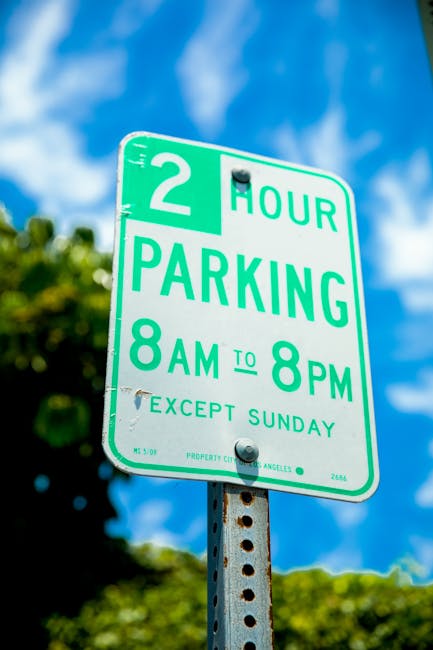 A close-up view of an asphalt parking space featuring a yellow painted accessibility symbol for disabled parking, positioned on the ground outside a residential property. Surrounding the symbol are ot